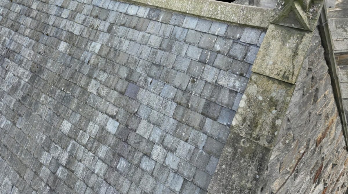 Close view of weathered roof slates, a stone ridge coping and a carved finial on a church roof, from a Droneacres 3D model